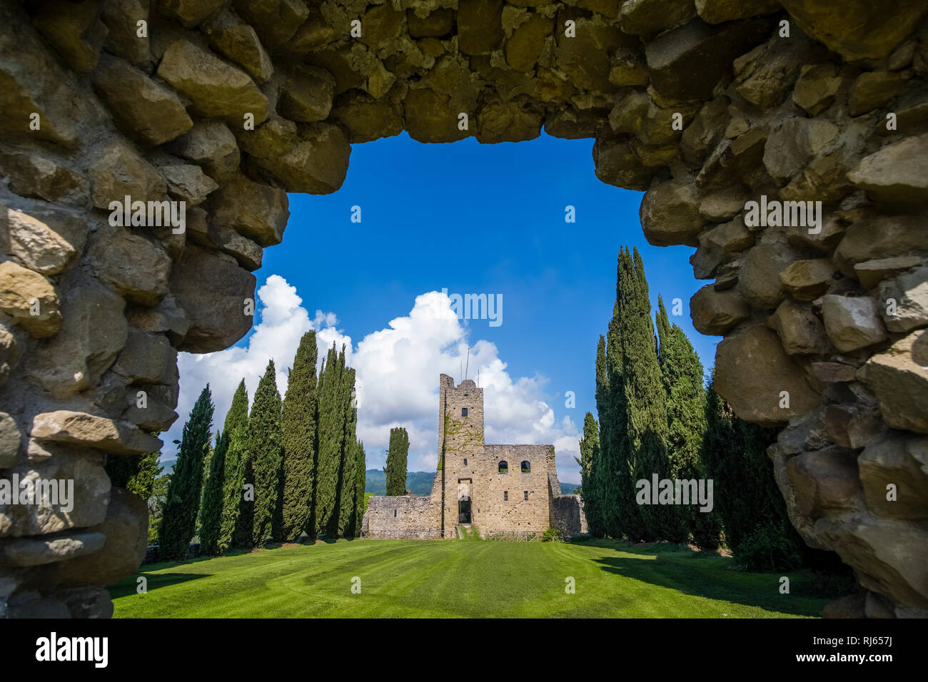 Castello di Romena si trova sulla cima di una collina, incorniciata da cipressi, visto attraverso un cancello roccioso Foto Stock