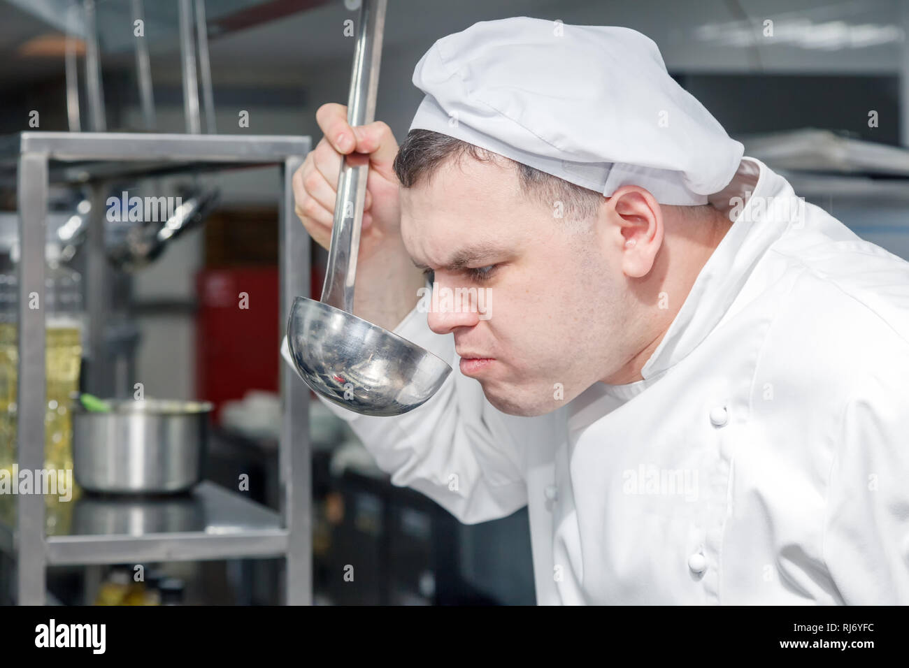 Closeup ritratto uomo chef professionale in bianco uniforme sta cercando piatto fatto fuori del mestolo. Concetto di controllo di qualità nel ristorante, il de Foto Stock