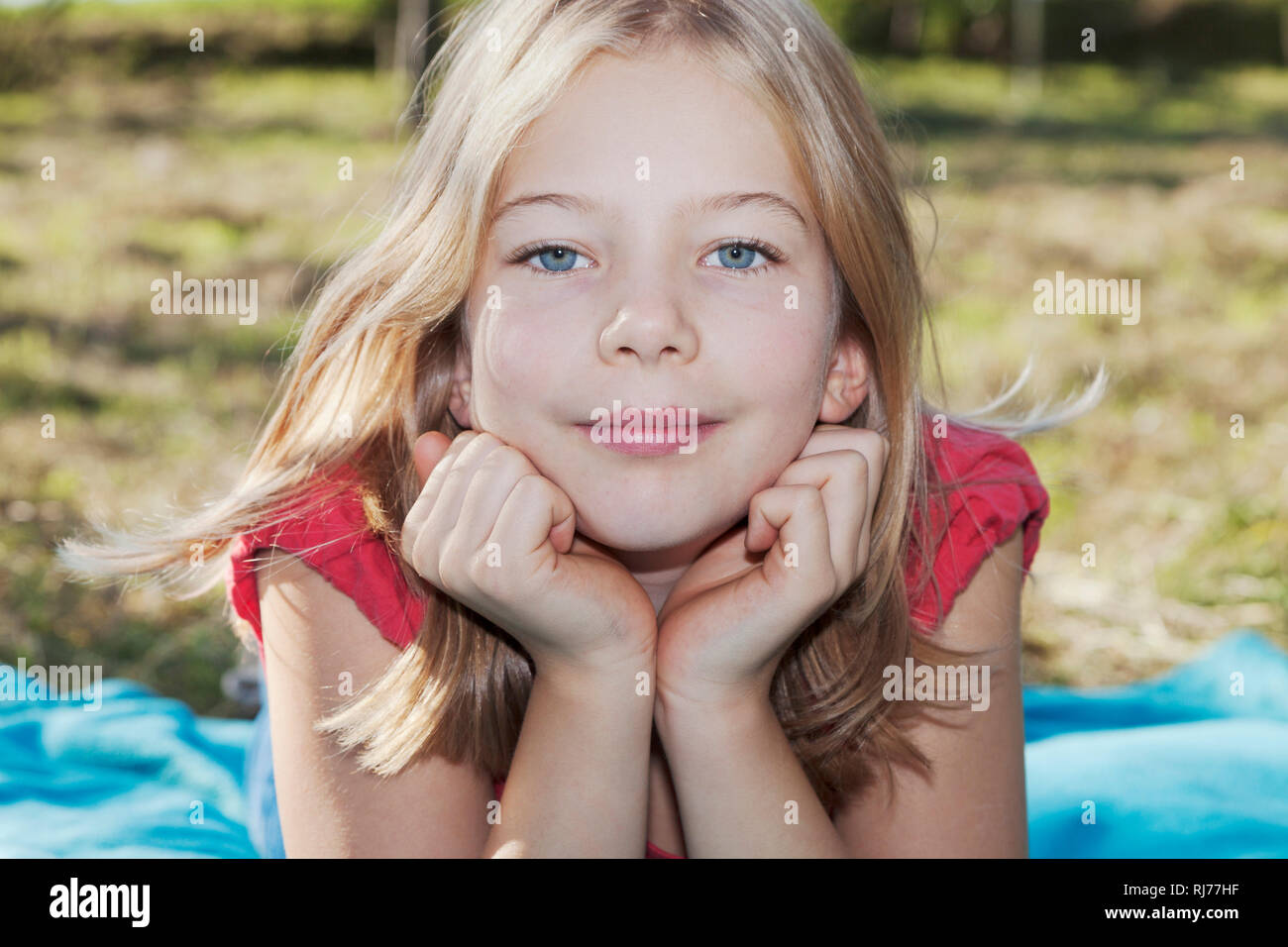 Portrait eines neunjähriges Mädchen auf einer Wiese, Kopf in die Hände gestützt Foto Stock