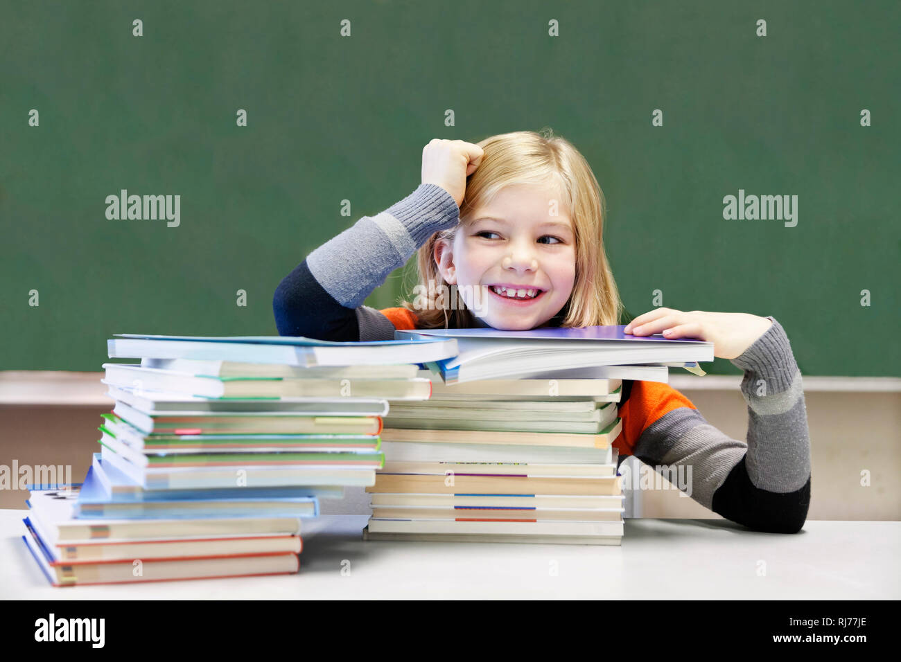 Schülerin, 9 Jahre alt, lächelnd vor zwei Stapeln Bücher vor einer Tafel Foto Stock