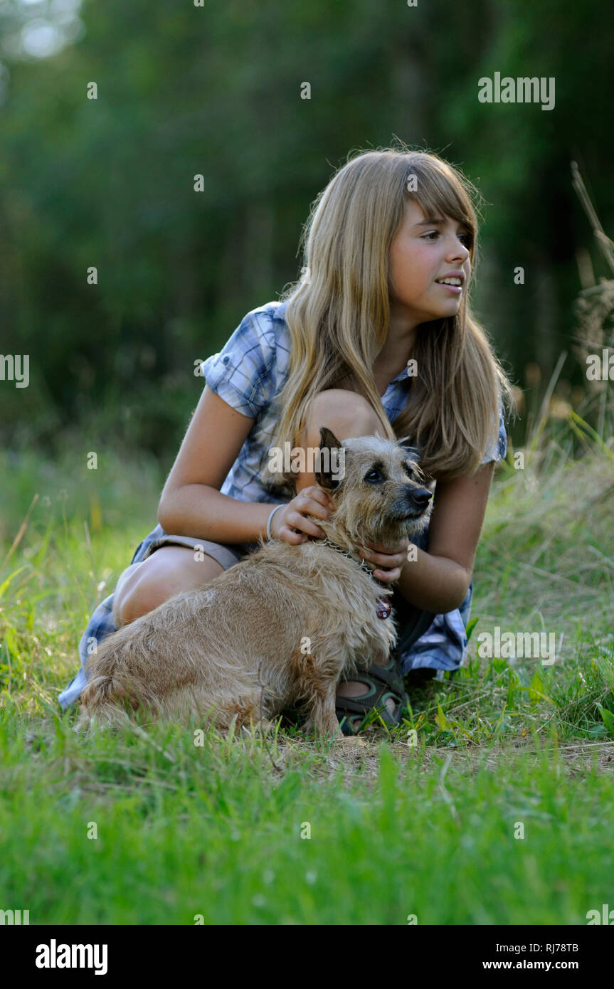 Mädchen und kleiner Mischlingshund auf einer Wiese, Blick zur Seite, Hintergrund unscharf Foto Stock