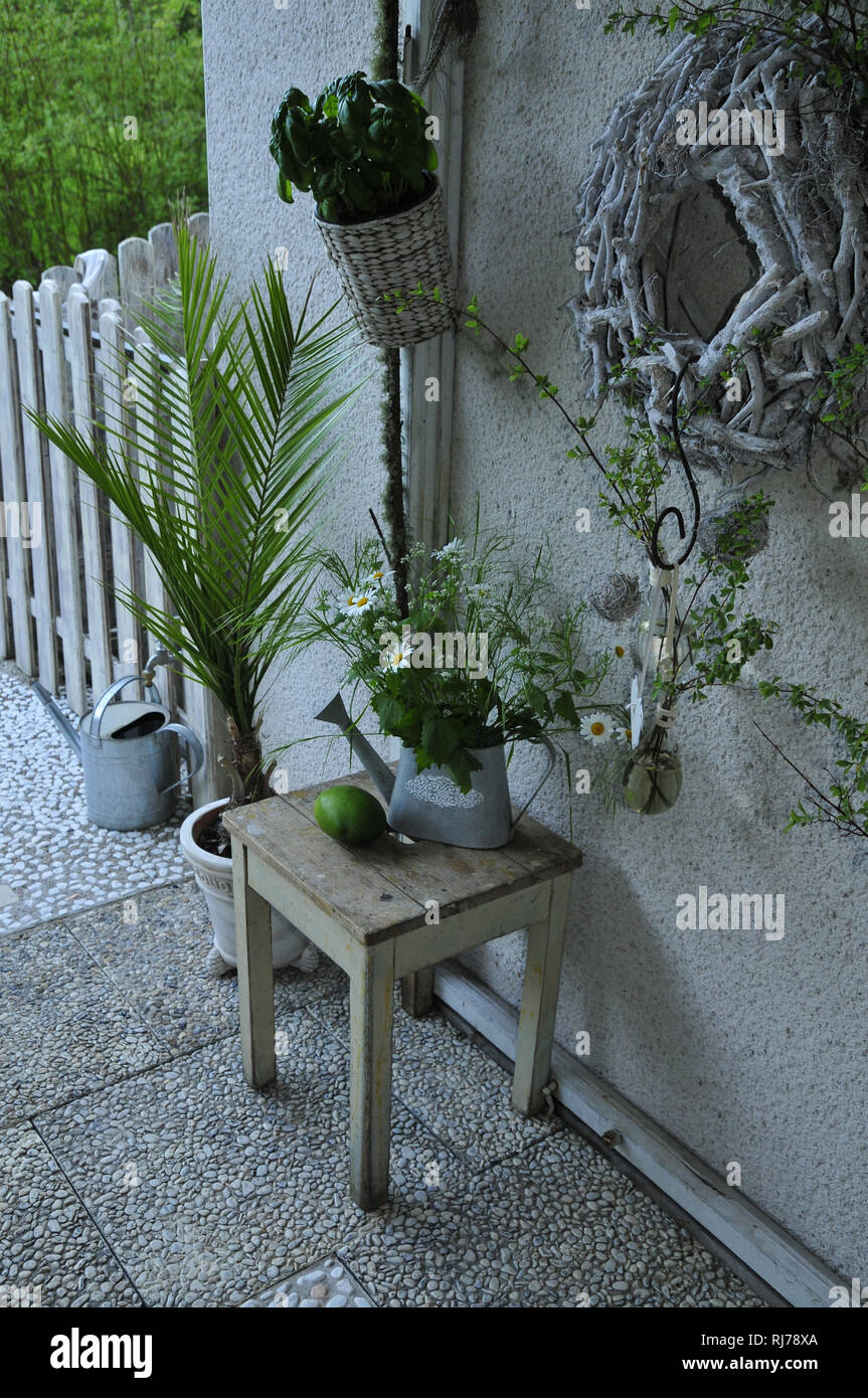 Terrassendeko mit Hocker, Kranz und Wiesenstrauß in alter Gießkanne, in weiß- und Grüntöne Foto Stock