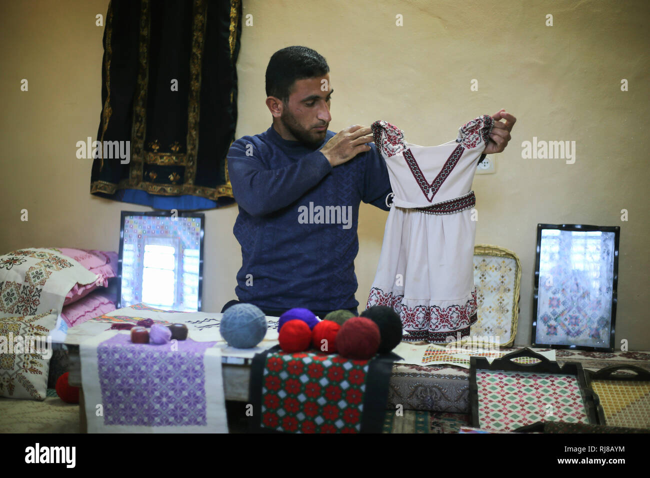 Suleiman guardando un abito durante come lavora. Giovani palestinesi uomo Suleiman Abu Taima 23 anni ha ereditato la professione di ricamo da sua madre e di lavorare in assenza di opportunità di lavoro e il peggioramento della situazione economica e l'assedio alla Striscia di Gaza. Foto Stock