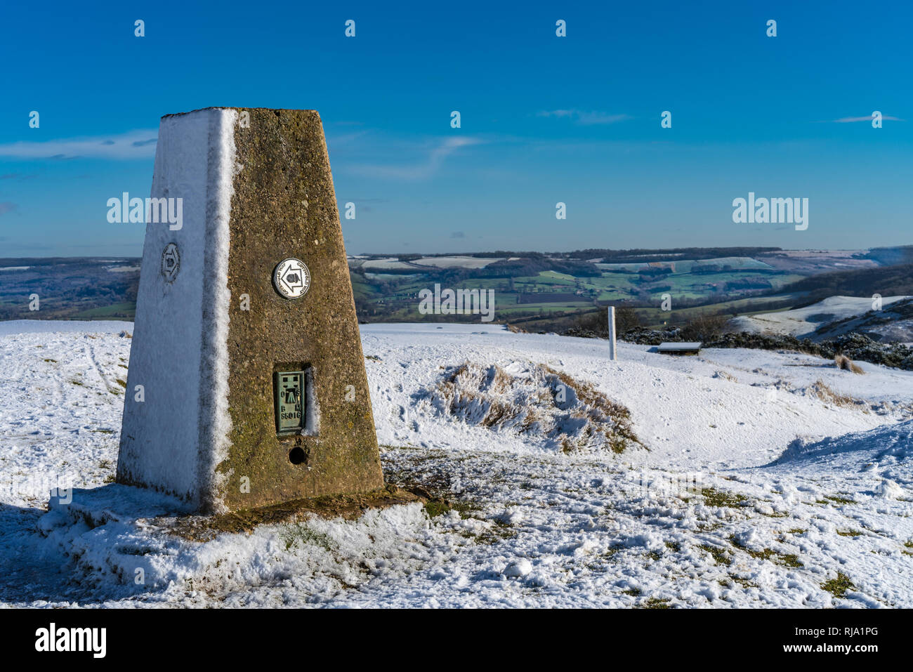 Vista dal vertice di Cleeve Hill sul Cotswold Way, Gloucester Regno Unito compreso il trig marcatore punto coperto di neve in inverno Foto Stock