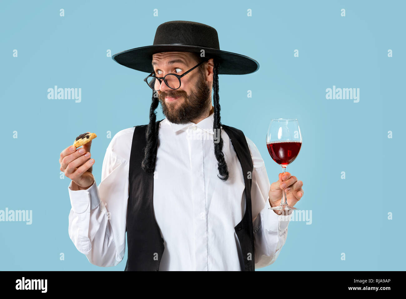 Il giovane ebrea ortodossa uomo con cappello nero con Hamantaschen i cookie per la festa ebraica di Purim in studio. La festa di Purim, ebraica, festival, vacanze, celebrazione, ebraismo, pasticceria, tradizione, cookie, il concetto di religione Foto Stock