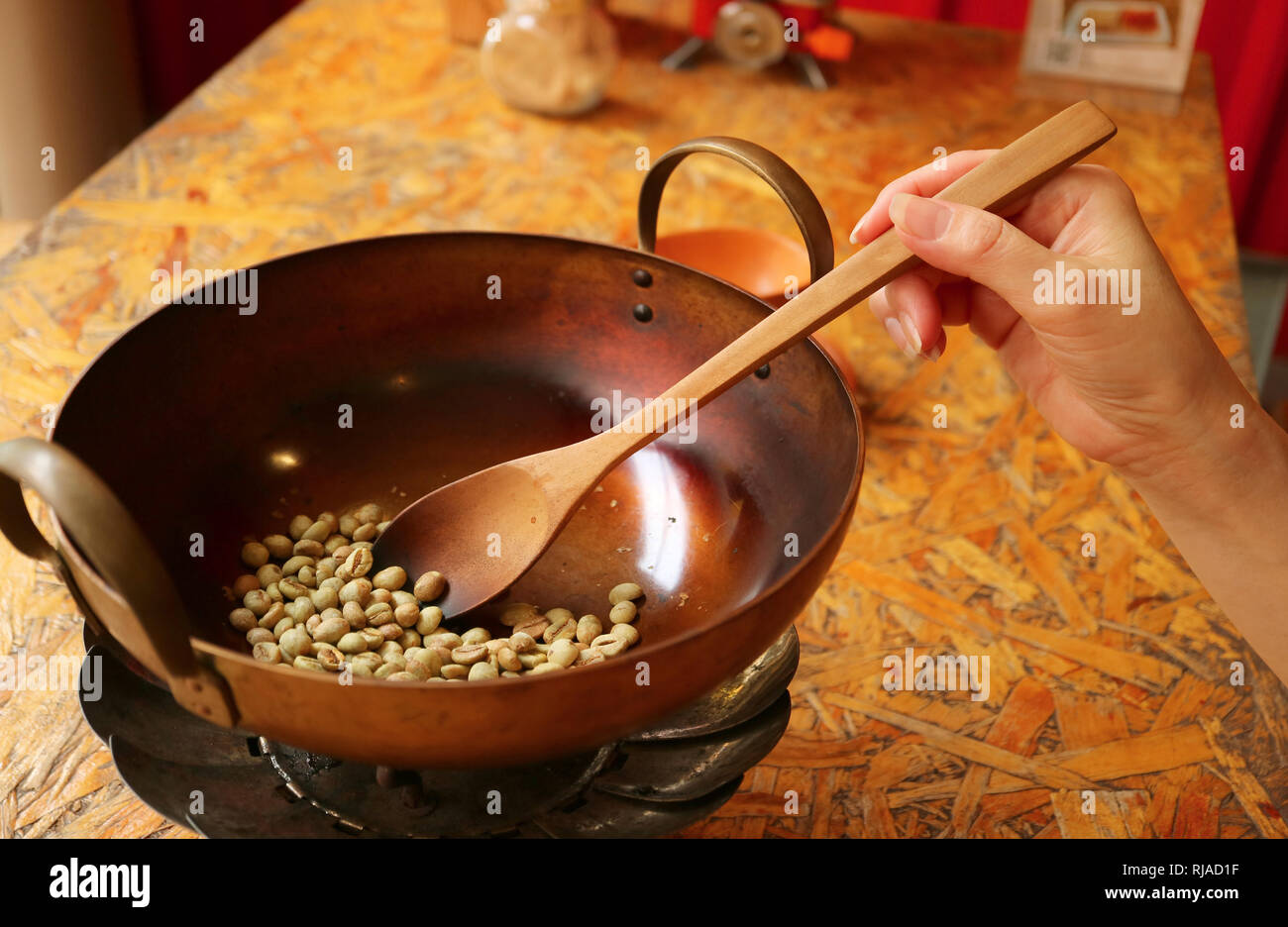 Donna di mano con una forcella di legno grezzo di tostatura i chicchi di caffè in una coppa di ottone per il caffè fatti in casa Foto Stock
