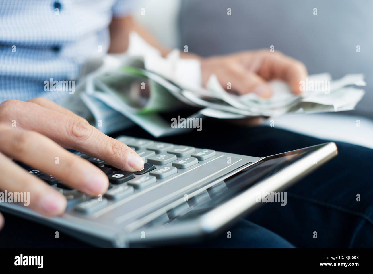 Primo piano di un uomo caucasico con una pila di banconote e biglietti nella sua mano utilizzando un calcolatore elettronico per fare alcuni conti Foto Stock