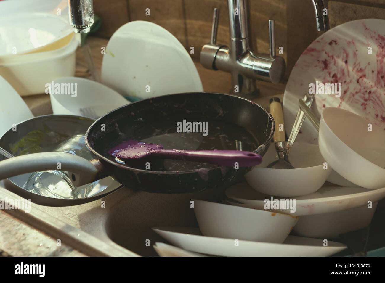 Un mucchio disordinato di piatti sporchi e utensili in lavello da cucina Foto Stock