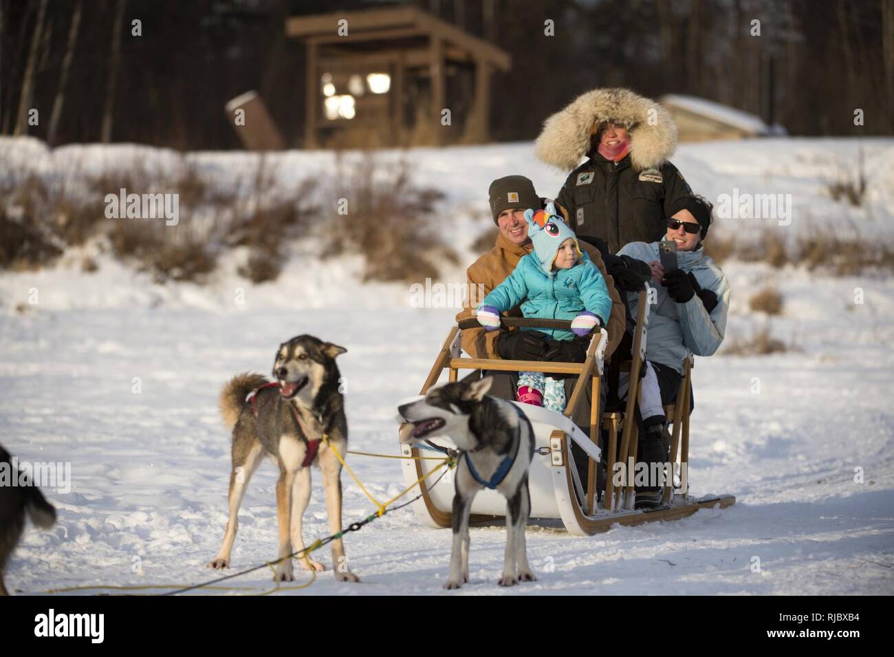 La famiglia Novak, da Philadelphia, Pa., passa per una slitta trainata da cani giro sul lago Hillberg a base comune Elmendorf-Richardson, Alaska, 14 gennaio 2018. Coast Guard Lt. Michael Novak è stazionato a JBER. Come parte della morale, il benessere e la ricreazione programma ospitato dal 673d forza squadrone di supporto e vita JBER Team, il Hillberg Ski Area offre quelli con accesso di base di una varietà di sport invernali e gli eventi. Foto Stock