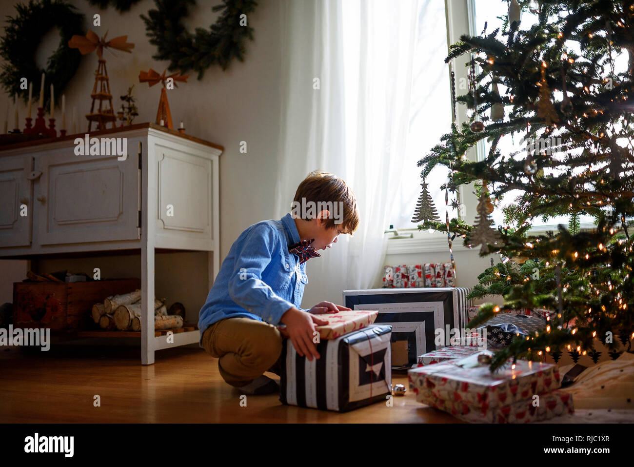 Ragazzo in ginocchio di fronte a un albero di Natale guardando doni Foto Stock