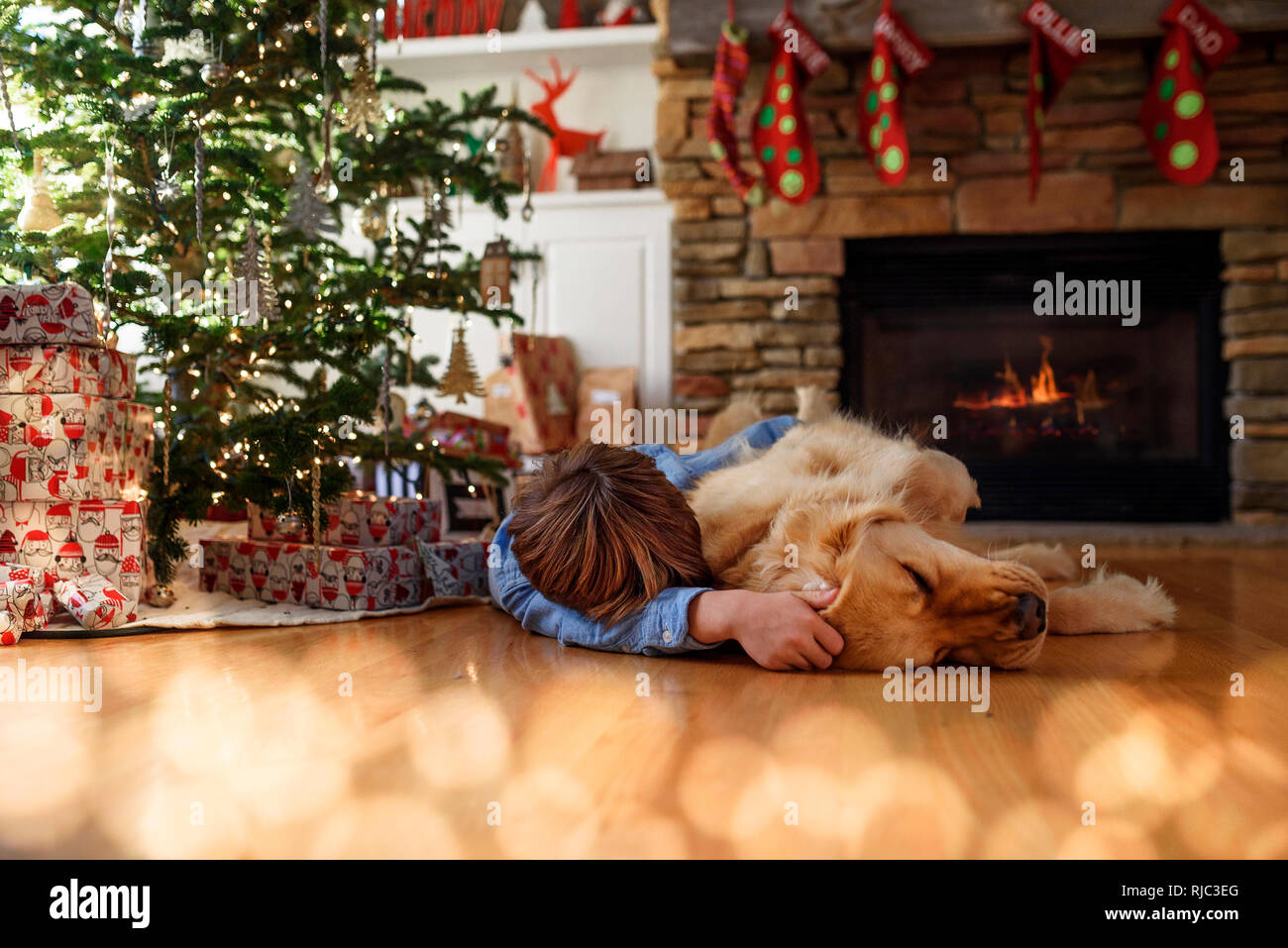 Ragazzo disteso sul pavimento nella parte anteriore di un albero di Natale cuddling il suo cane Foto Stock