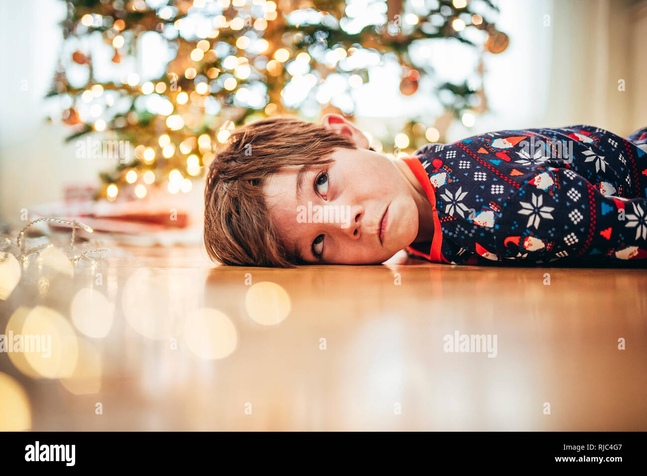 Ragazzo disteso sul pavimento nella parte anteriore di un albero di Natale tirando funny faces Foto Stock