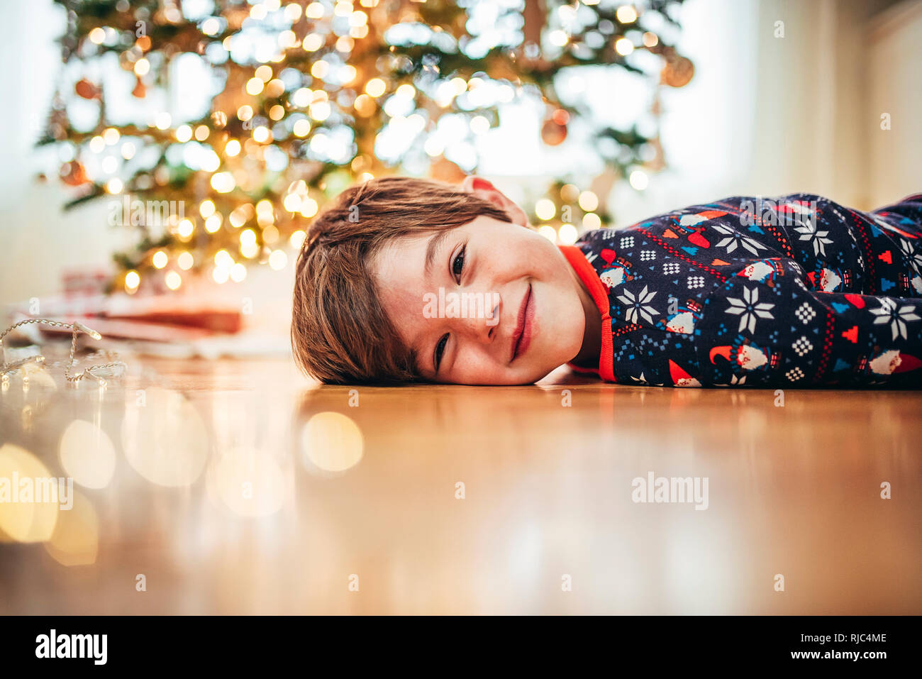 Sorridente ragazzo disteso sul pavimento nella parte anteriore di un albero di Natale Foto Stock