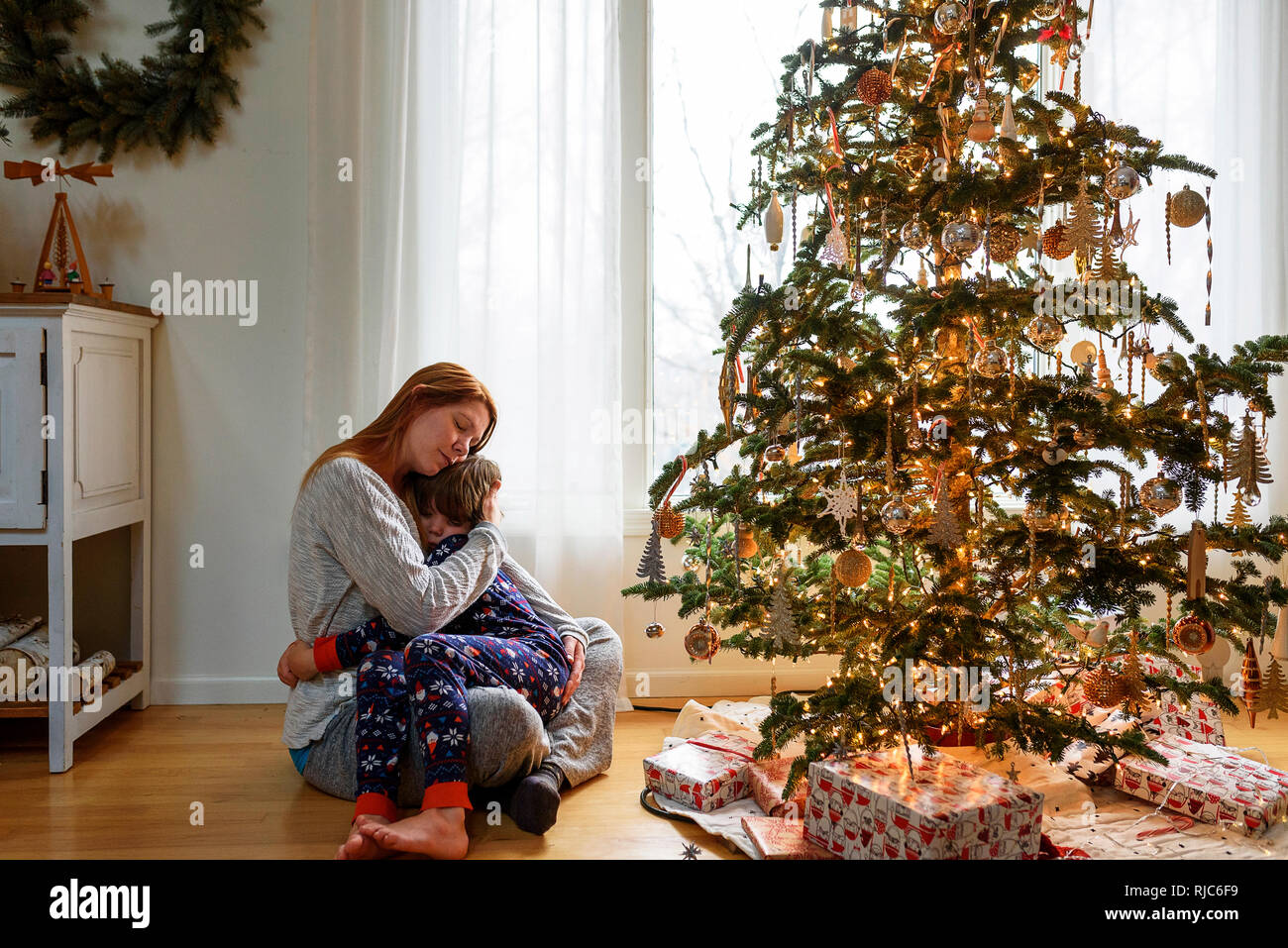 Donna seduta con un albero di Natale che abbraccia il suo figlio Foto Stock