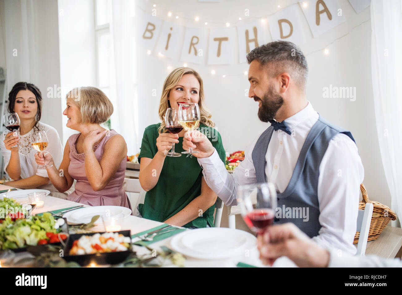 Una grande famiglia seduti a un tavolo in una piscina festa di compleanno, bicchieri tintinnanti. Foto Stock