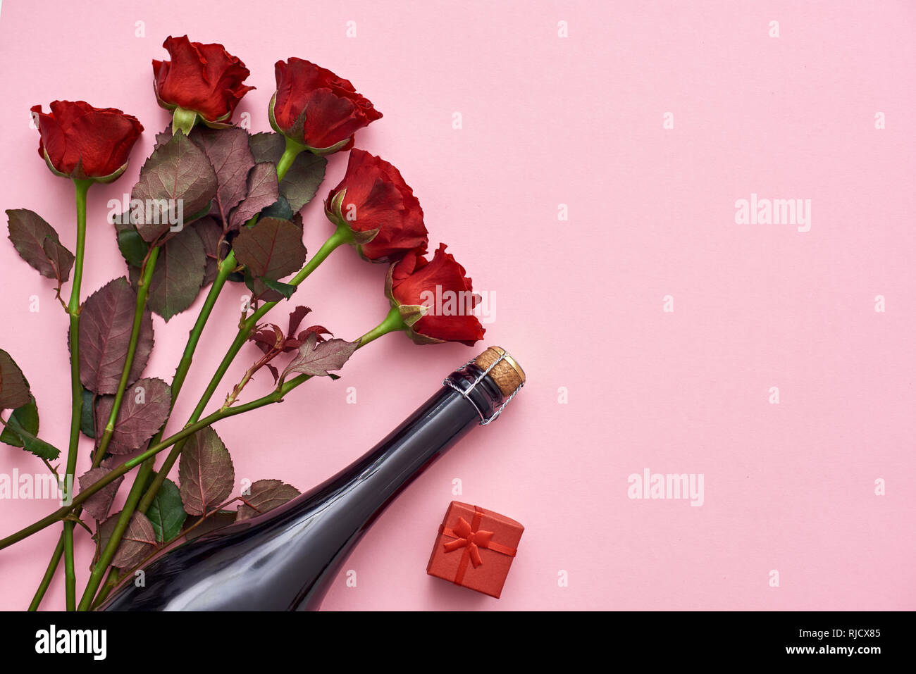 Celebrare la data speciale. Sorprenderla con rose rosse, champagne e piccola confezione regalo rossa. Sfondo rosa Foto Stock
