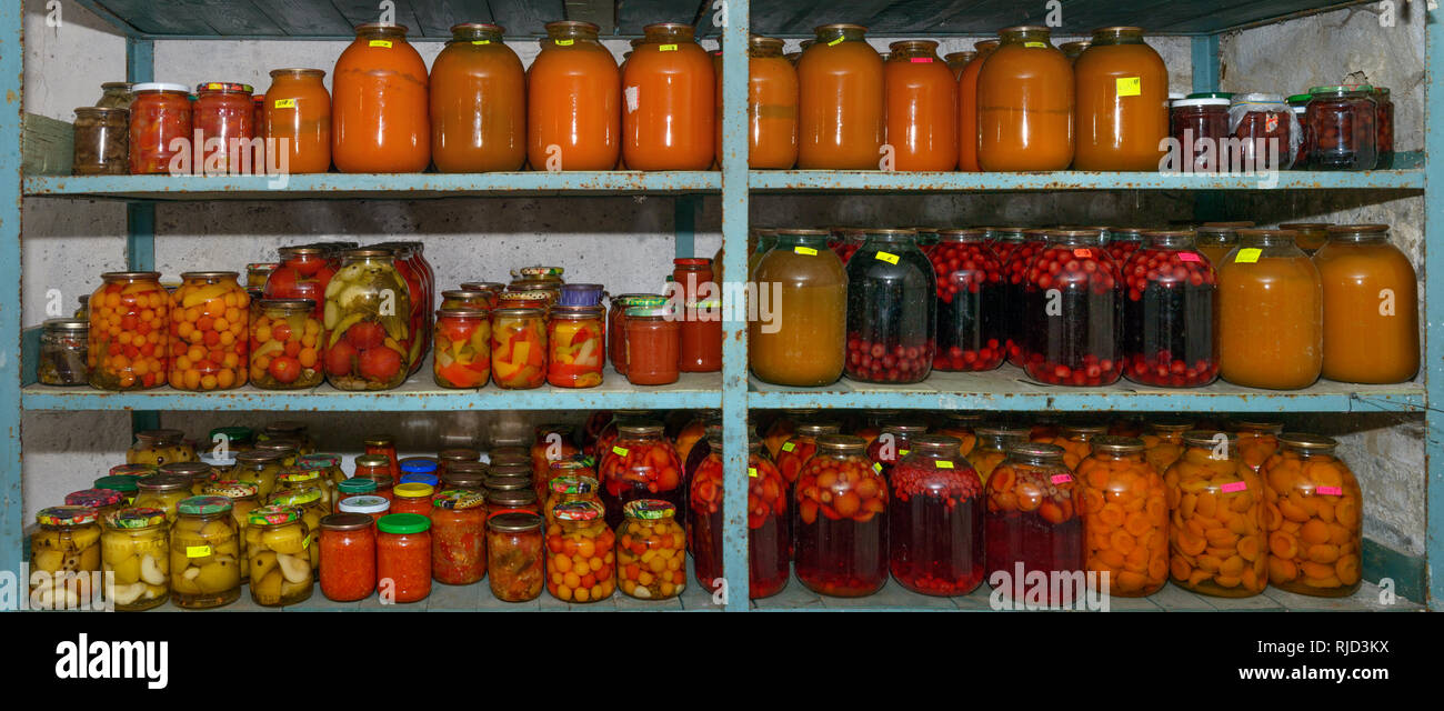 Close-up scaffali con molti vasi di home-conserve di disposizioni di colore rosso brillante e di colore arancione nella cantina di casa. Foto Stock