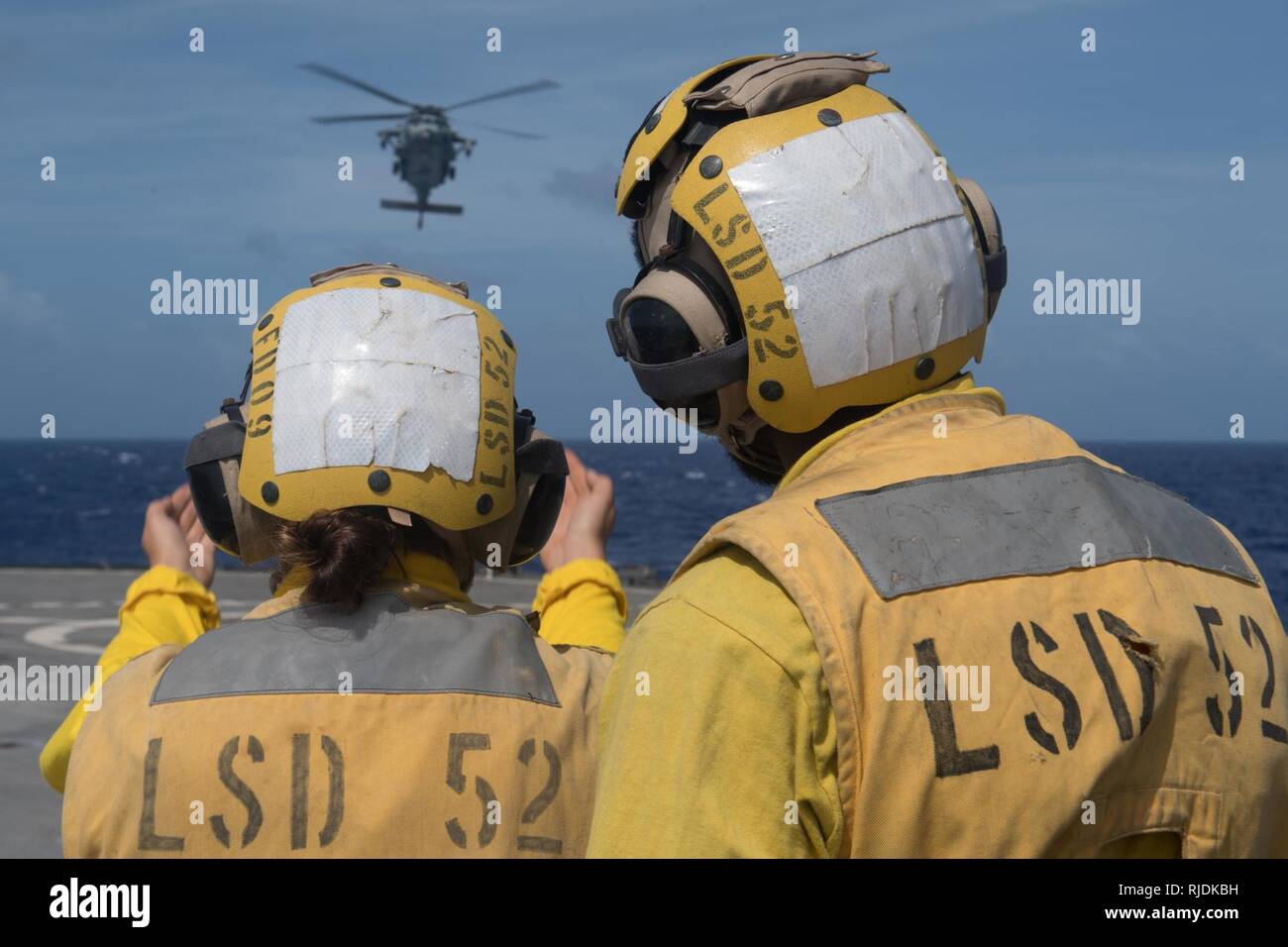 Oceano Pacifico (GEN. 12, 2018) di Boatswain Mate 3° di classe Taryn Jewett, sinistra, assegnato al dock di anfibio sbarco nave USS Pearl Harbor (LSD 52), guide un MH-60S Sea Hawk elicottero assegnato al "Jolly" di elicottero di mare squadrone di combattimento (HSC) 23, dalla nave del ponte di volo. Pearl Harbor è parte dell'America anfibio gruppo pronto, che è operativo nel Indo-Asia-regione del Pacifico per rafforzare i partenariati e servire come una pronta risposta in vigore per qualsiasi tipo di emergenza. Foto Stock