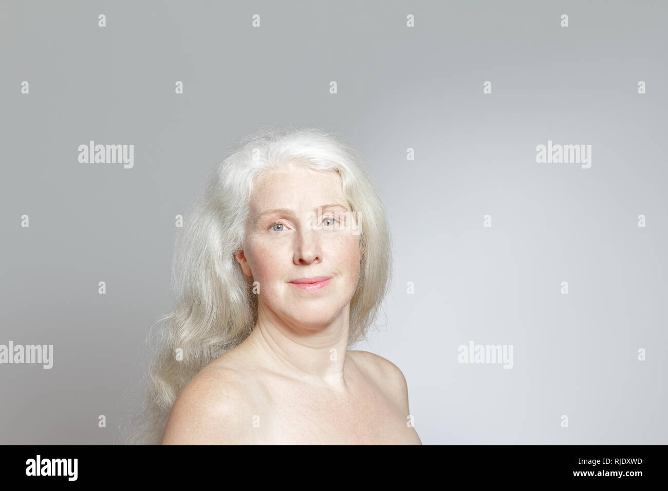 Colpo di testa di un attraente donna matura con belle lunghi capelli grigi davanti a uno sfondo bianco, copia dello spazio. Foto Stock