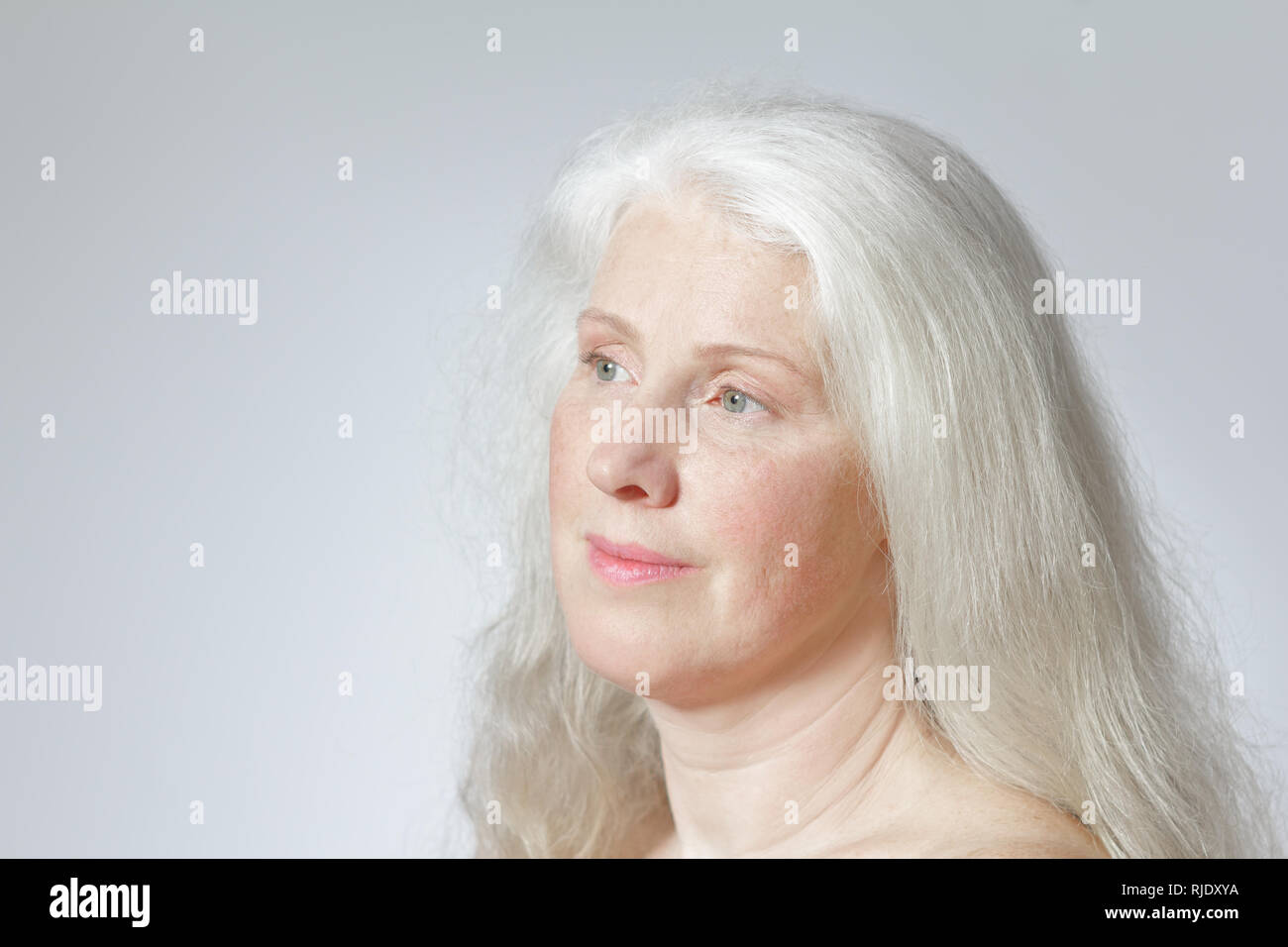 Colpo di testa di un attraente donna matura con belle lunghi capelli grigi davanti a uno sfondo bianco, copia dello spazio. Foto Stock