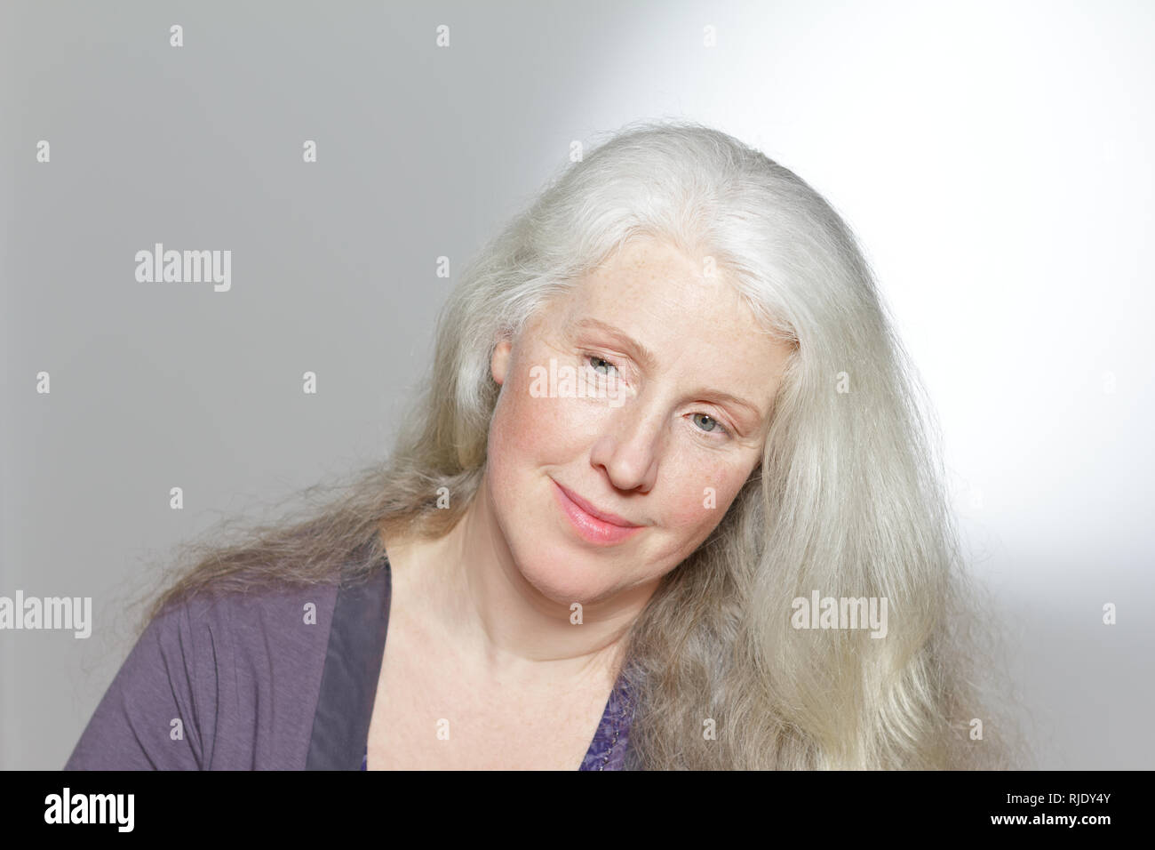 Colpo di testa di un attraente donna matura con belle lunghi capelli grigi davanti a uno sfondo bianco, copia dello spazio. Foto Stock