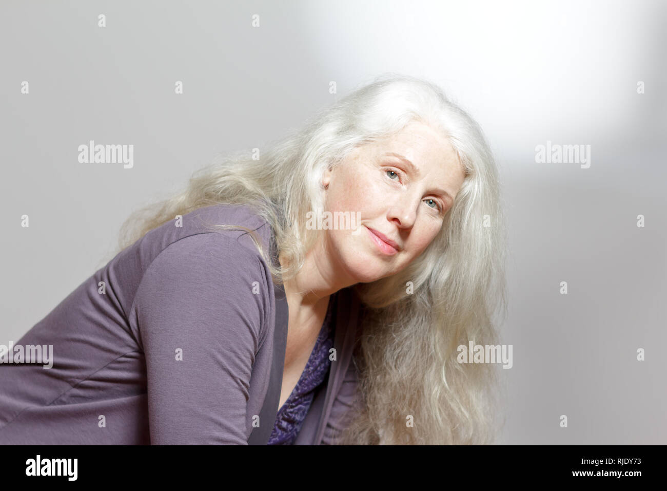 Colpo di testa di un attraente donna matura con belle lunghi capelli grigi davanti a uno sfondo bianco, copia dello spazio. Foto Stock