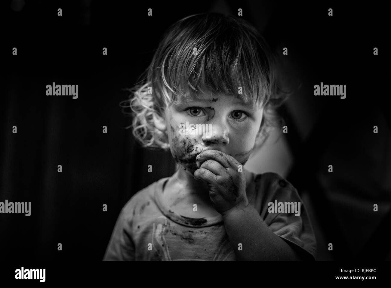 Un ritratto in bianco e nero di un simpatico ragazzo caucasico con una faccia sporca di mangiare una pillola di carbone di legna. Isolato su sfondo nero Foto Stock