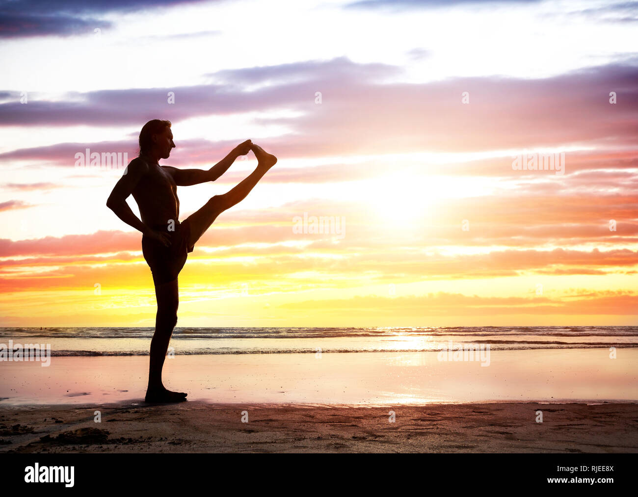 Montare l'uomo in silhouette a fare yoga sulla spiaggia vicino all'oceano al tramonto in India Foto Stock