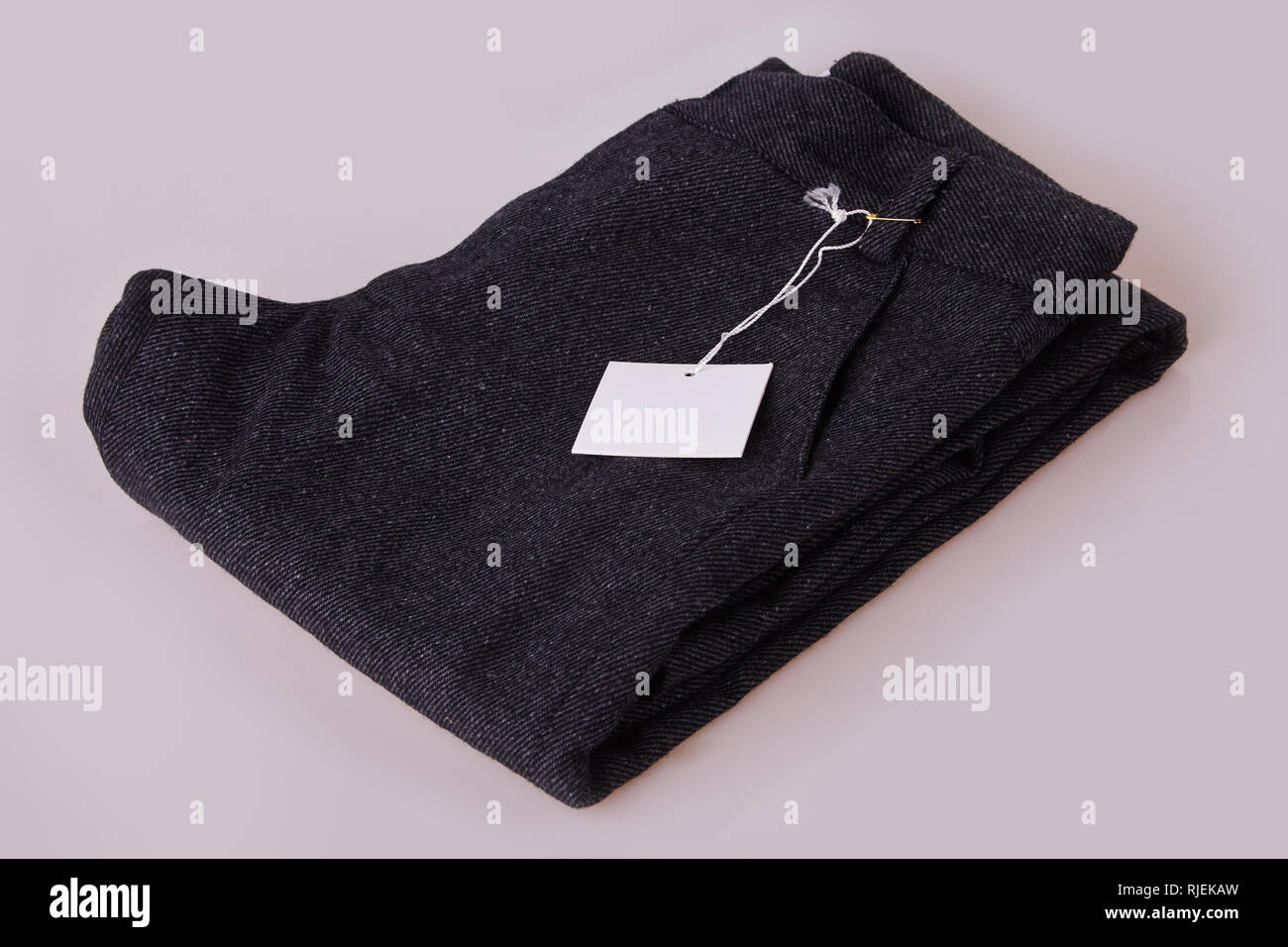 Organici grigio scuro pantaloni. Pantalone pila su uno sfondo bianco. Abbigliamento tag. Carta bianca prezzo tag etichetta Foto Stock