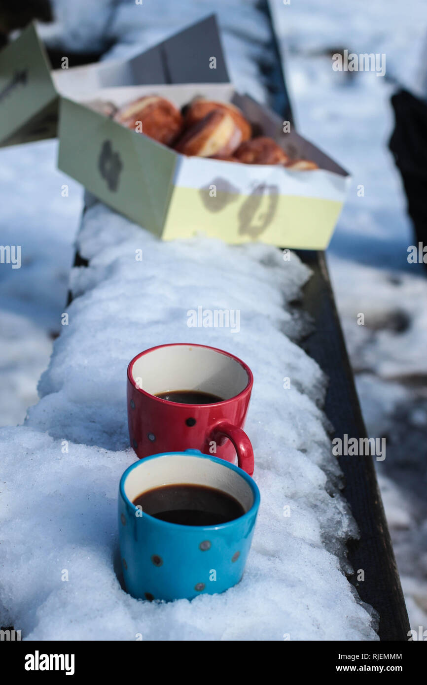 Due tazze di caffè e una ciambella sulla panchina coperta di neve Foto Stock
