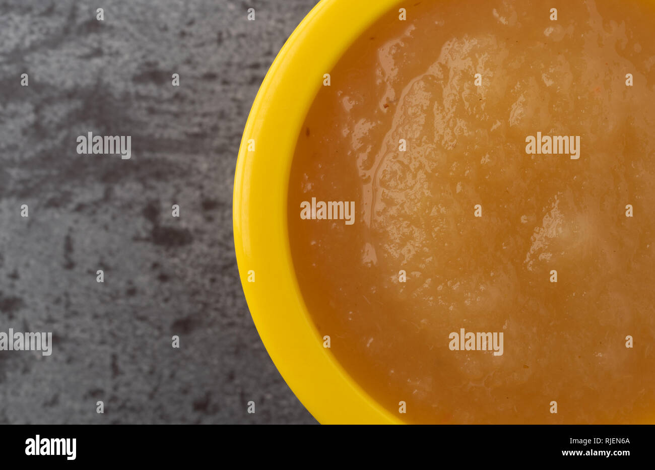 Tettuccio di chiudere la vista di un piccolo giallo ciotola riempita con salsa di mele su sfondo grigio. Foto Stock