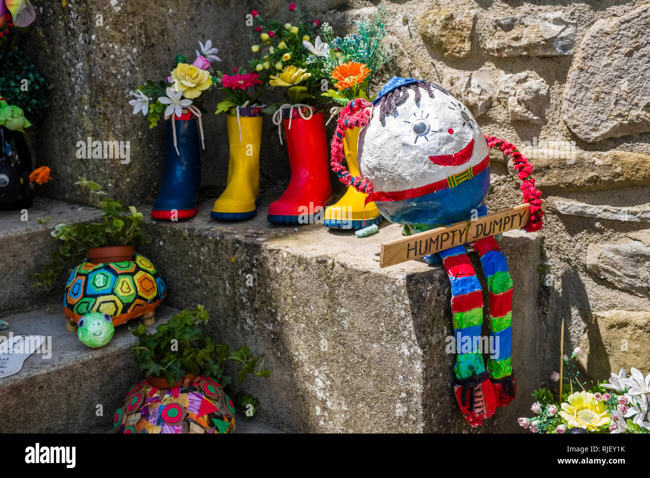 Decorazione colorata con scarpe di gomma, fiori e un burattino in corrispondenza di un ingresso di casa Foto Stock