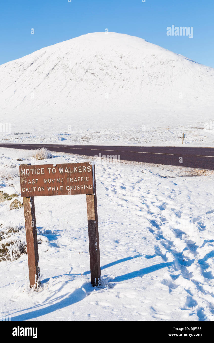Avviso per gli escursionisti in rapido movimento di traffico cautela durante l'attraversamento di firmare con la A82 road a Glencoe, altopiani, Scozia in inverno coperto di neve Foto Stock