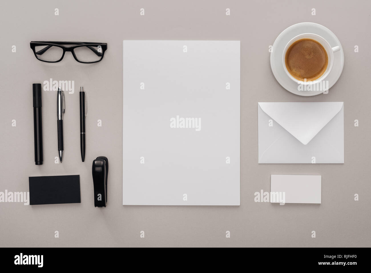 Lay piatto con occhiali neri, cancelleria e bianco le schede vuote al lavoro con la tazza di caffè su sfondo grigio Foto Stock