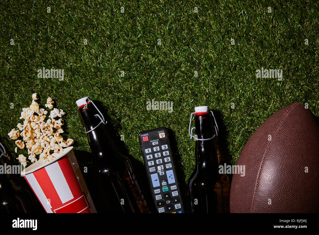 Piatto di laici bottiglie marrone nei pressi di pop-corn, il controllo remoto e la sfera sdraiati sull'erba Foto Stock