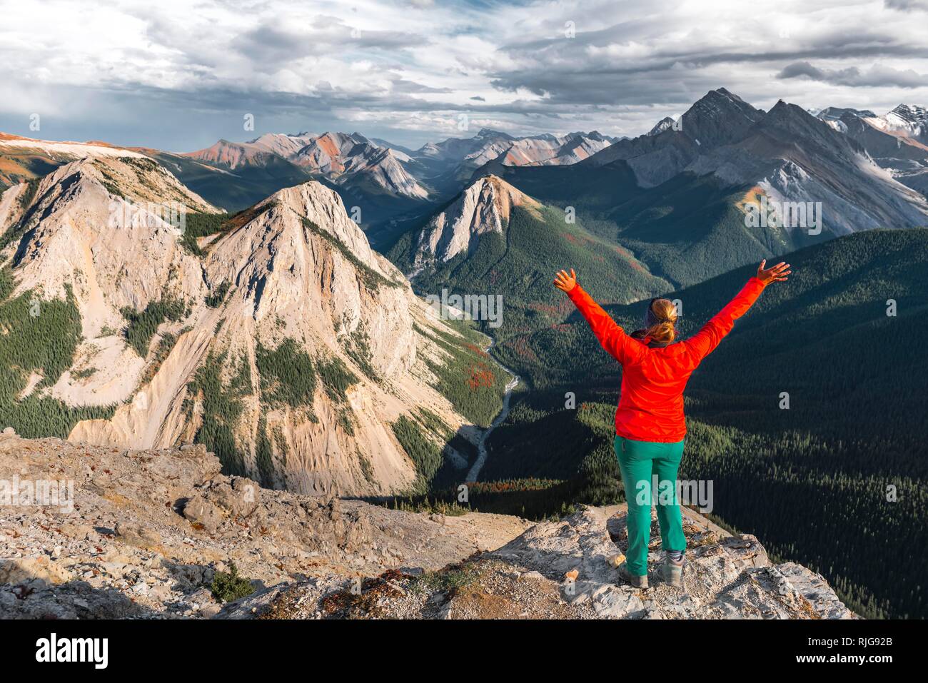 Escursionista femmina con i bracci sollevati cercando di vertice oltre il paesaggio di montagna, vertice con orange depositi di zolfo, Vista panoramica Foto Stock