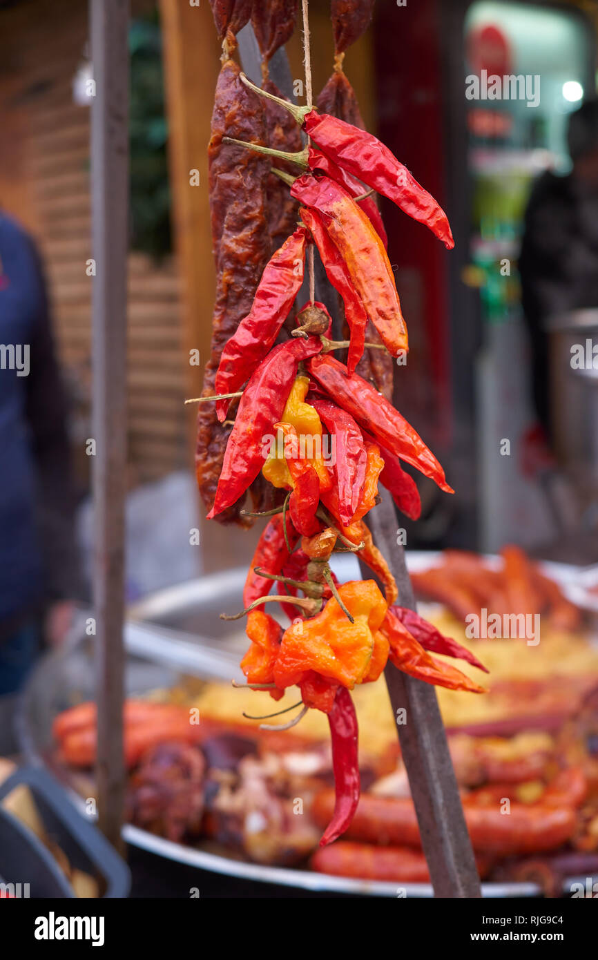 Red Hot peperoncini essiccati appeso di fronte a cottura lenta garretto (croato Buncek). Pressione di stallo di cibo al mercatino di Natale a Zagabria. Sfondo sfocato Foto Stock