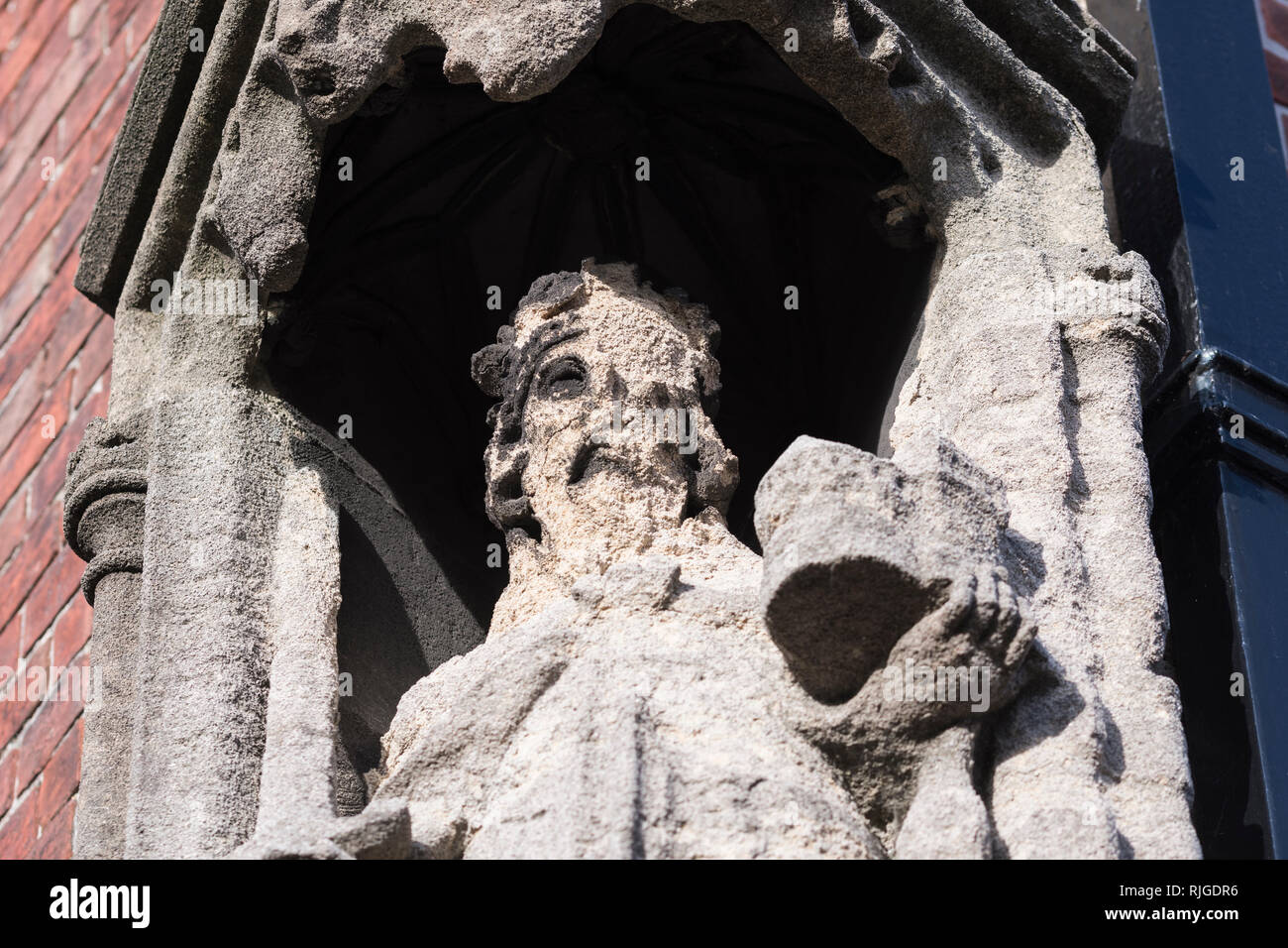 Epoca medievale storica statua di pietra in un'edicola su un angolo di un edificio di mattoni rossi, guardando molto spiovente e consumata in Arundel, West Sussex, Regno Unito. Foto Stock