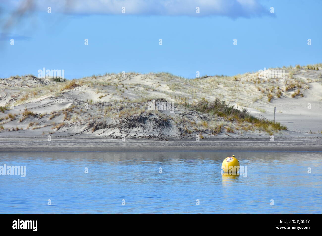 Sferica gialla 5 nodi di velocità boa limite sulla superficie calma del canale del porto con dune di sabbia in background. Foto Stock