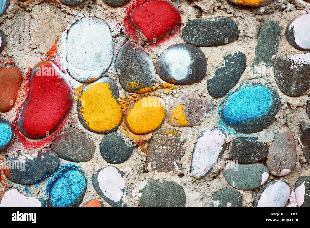 Verniciato colorato i ciottoli sulla superficie ruvida la superficie di un ciottolo muro di pietra Foto Stock