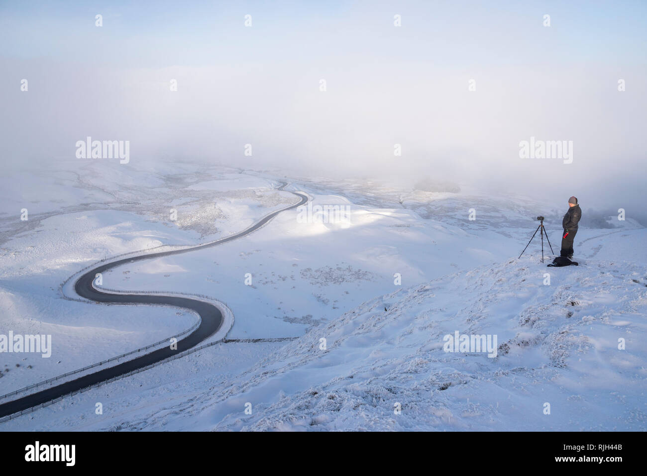 Fotografo sul Mam Tor nel parco nazionale del Peak District. Il ben noto bendy strada che conduce a Edale su un nevoso inverno mattina. Foto Stock