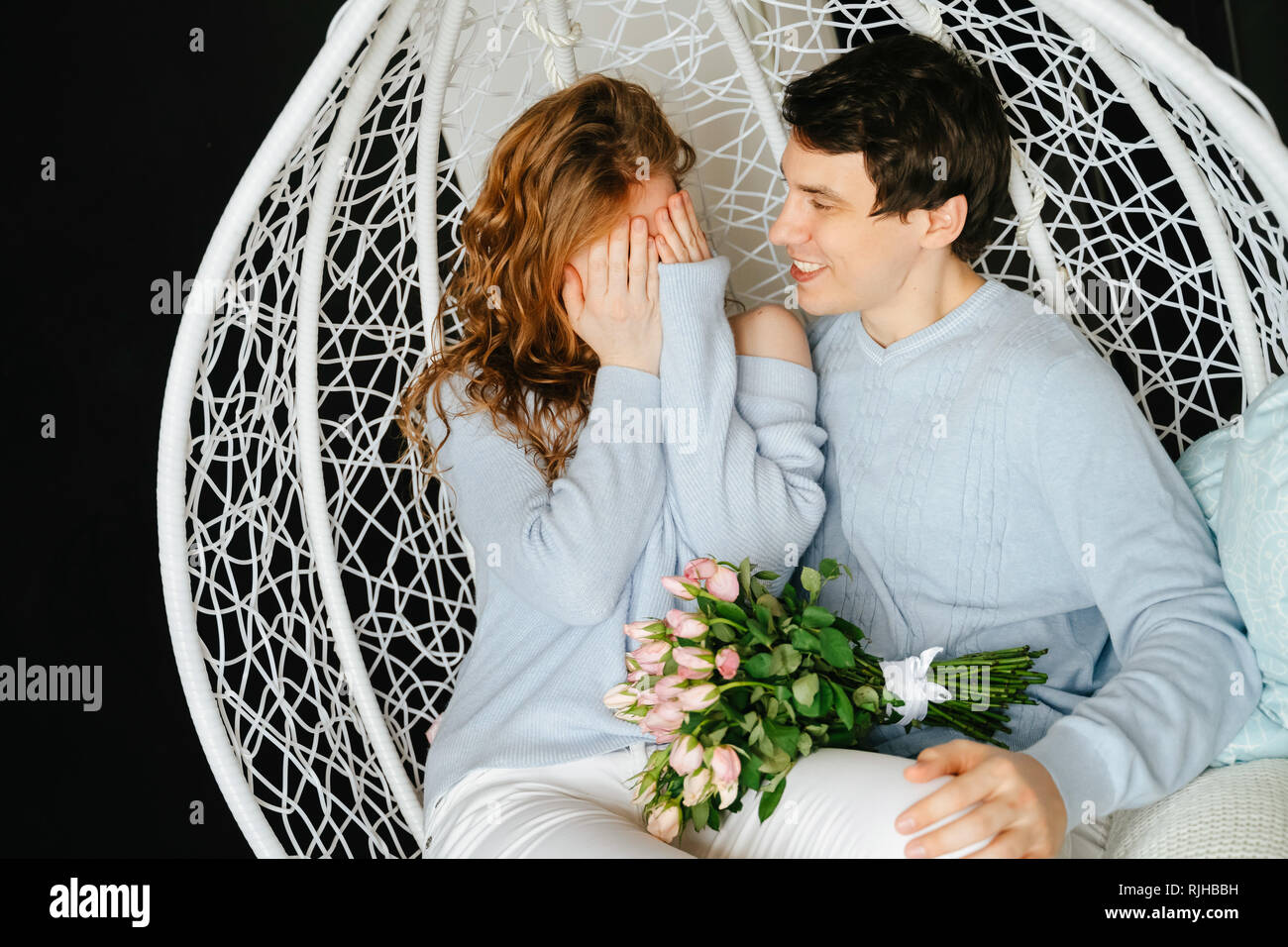 Giovane ragazza e guy avvolgente su una grande sedia con un bouquet di rose. Foto Stock