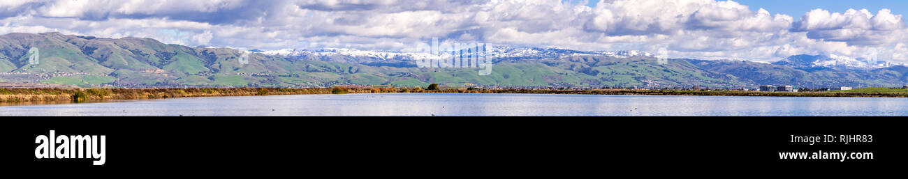 Vista panoramica verso il verde delle colline e montagne innevate in una fredda giornata invernale presi dalle rive di un laghetto nella parte sud di San Francisco Bay Area; San Jose, Foto Stock