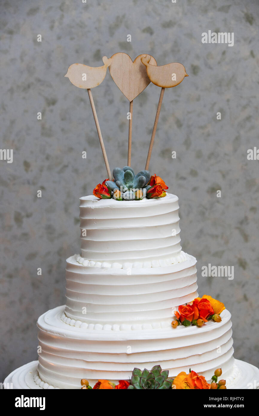 Bianco torta di nozze con arancio e giallo glassa fondente fiori e piante succulente con tre vuoto uccello in legno a forma di cuore topper Foto Stock