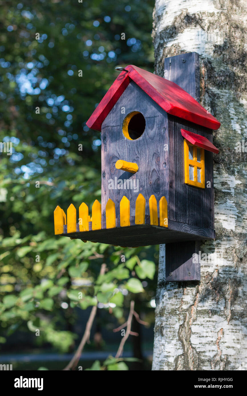Bird house con un tetto rosso, finestra di colore giallo e la recinzione su birch close up. L'immagine verticale Foto Stock