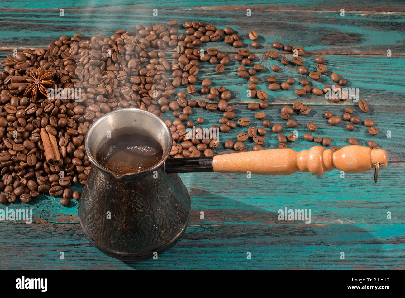 Caffè Fresco nel cezve (jezve) e sparse il caffè torrefatto in grani, cannella e anice stellato sul turchese tavolo in legno Foto Stock