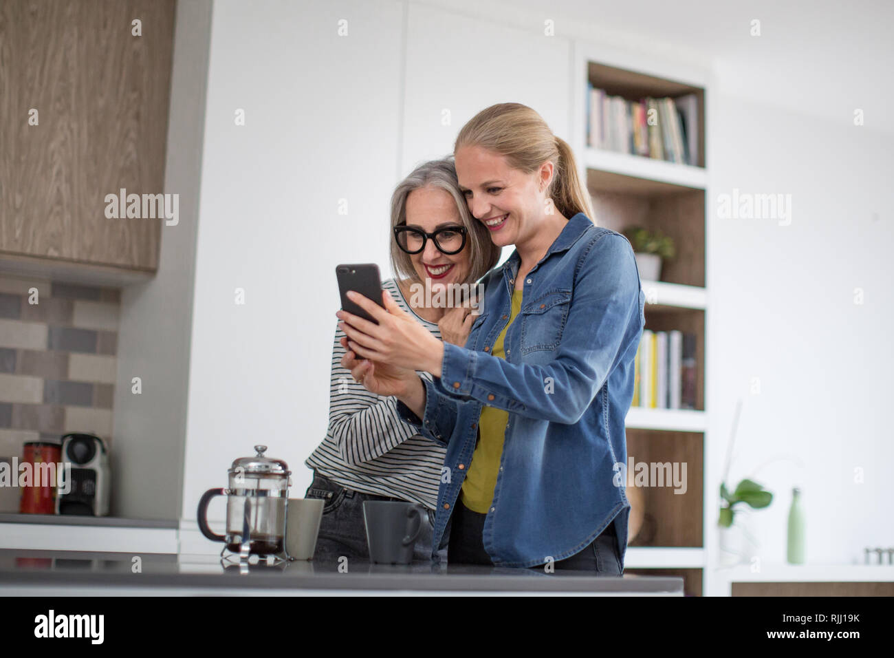 Coppia donna adulta con cresciuti figlia guardando smartphone in cucina Foto Stock