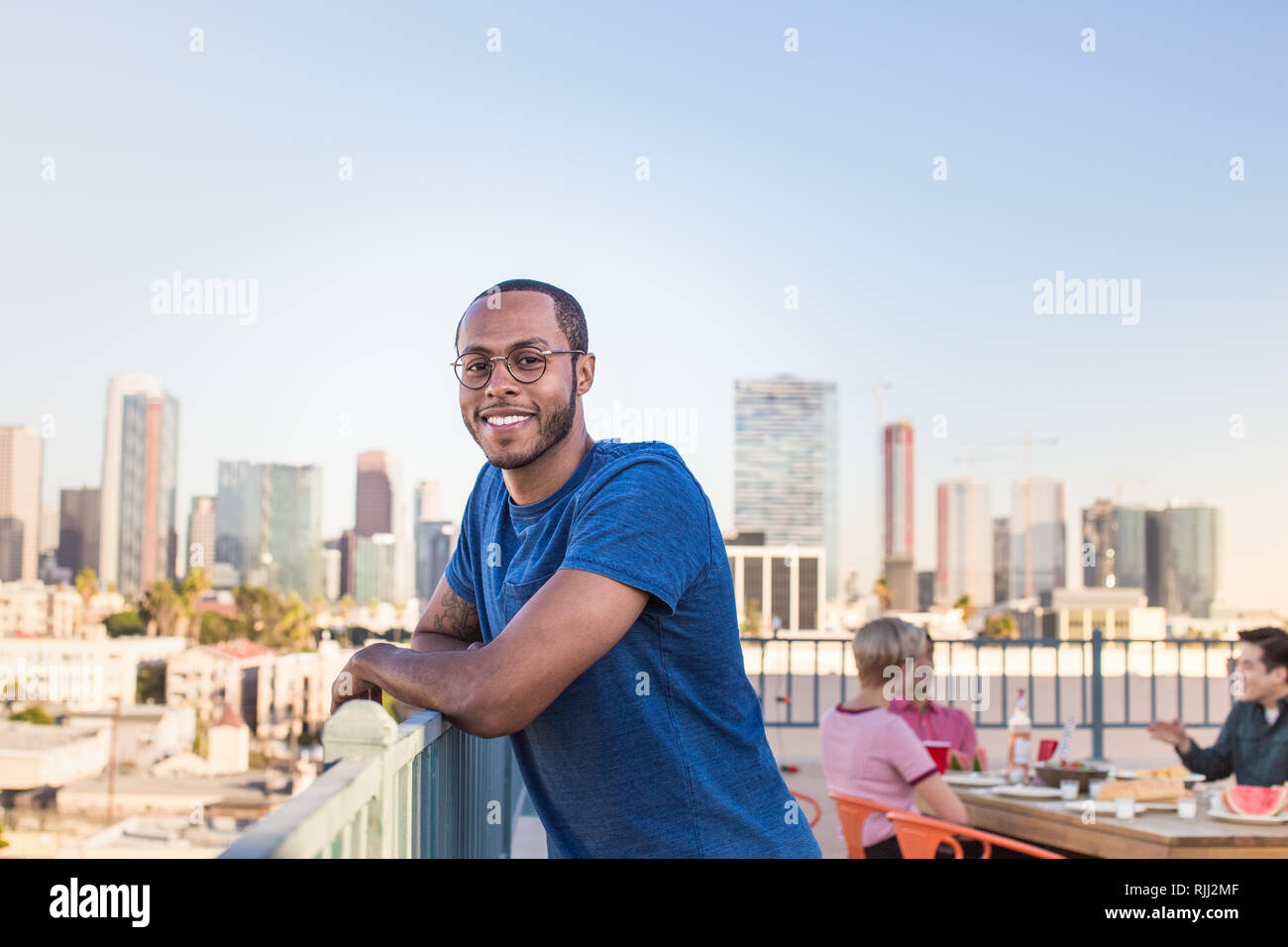 Ritratto di giovane adulto maschio a una festa sul tetto con lo skyline della città Foto Stock