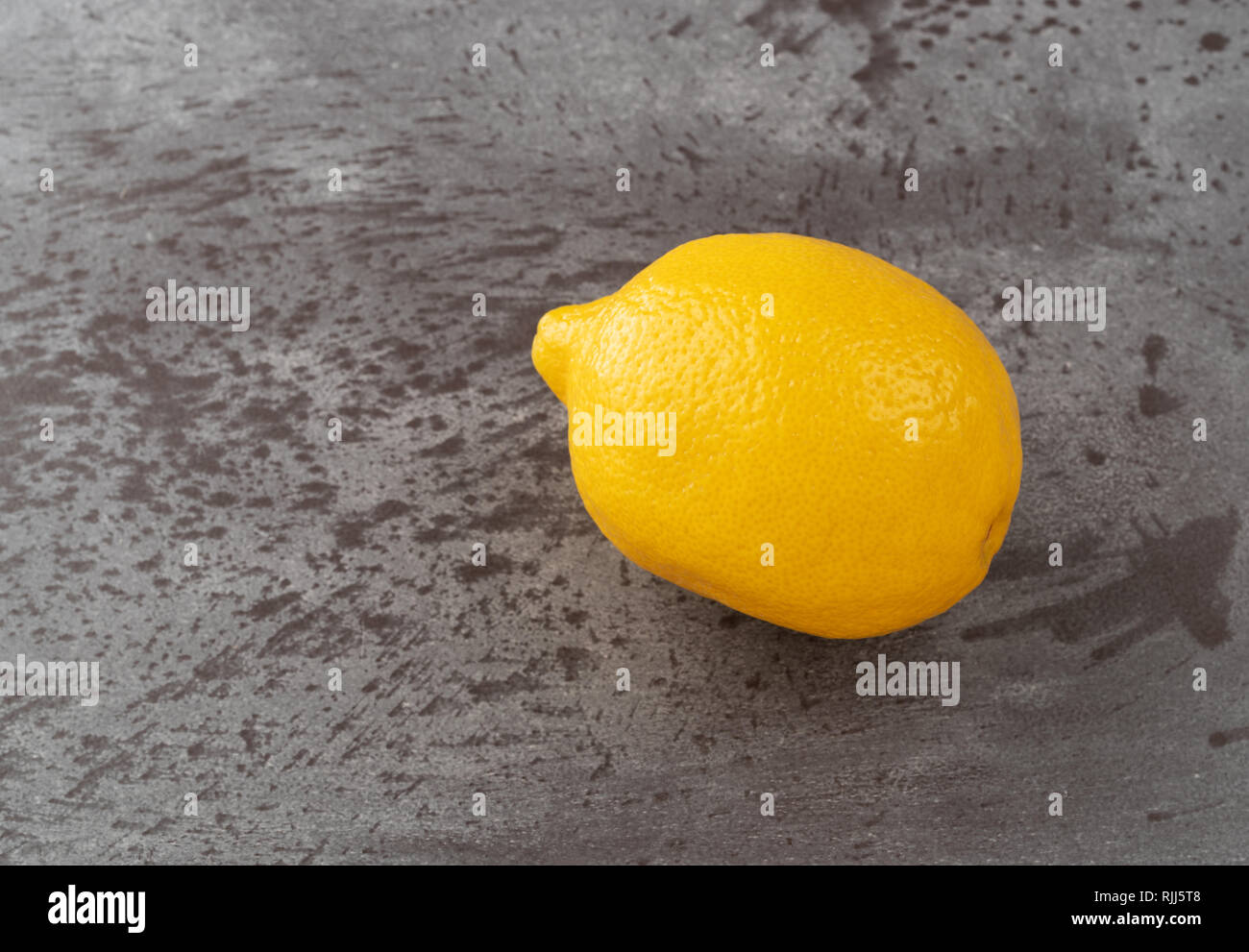 Vista laterale di un intero limone giallo su un contatore Gray top. Foto Stock