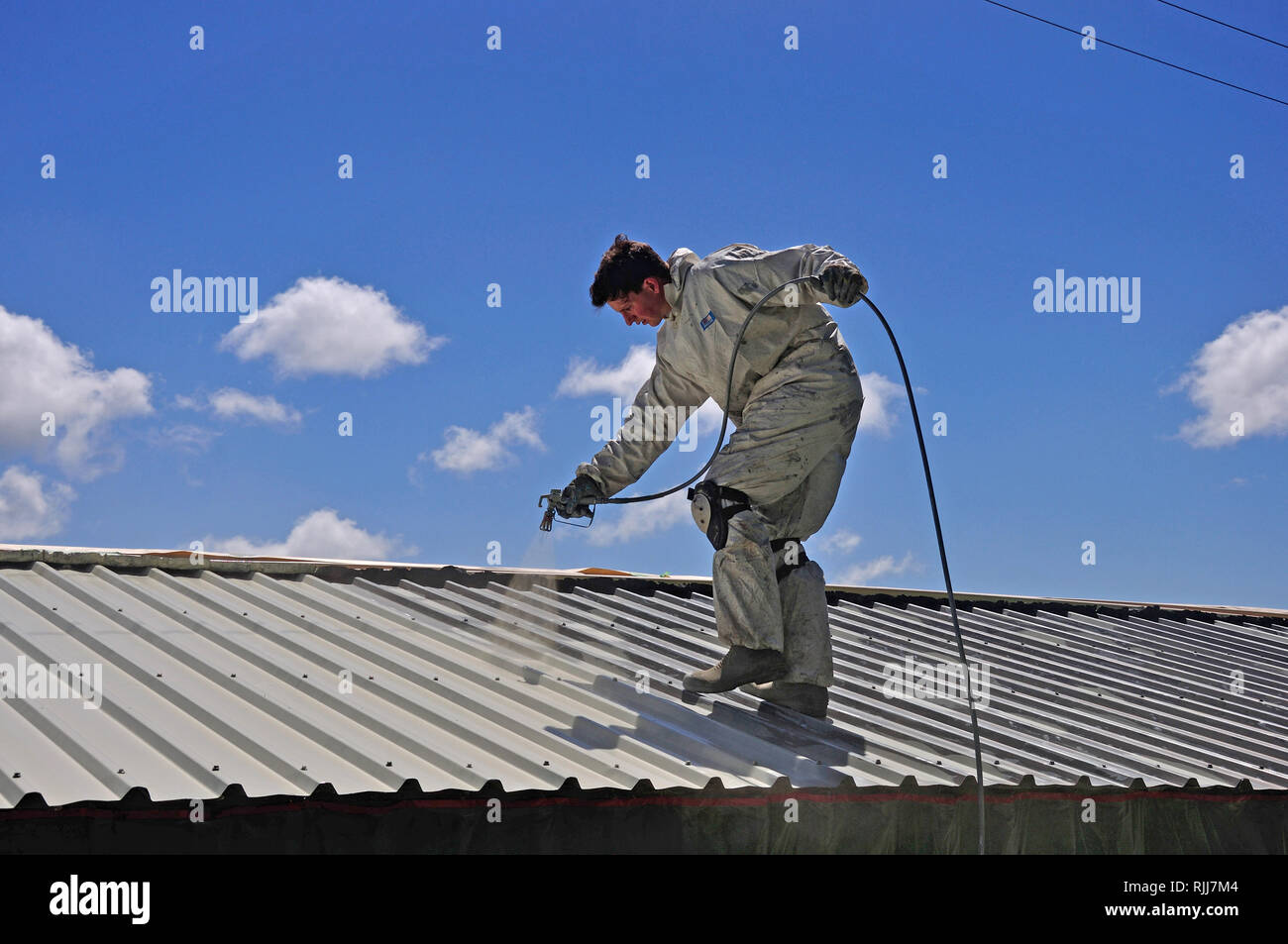 Un trademan utilizza un spruzzo airless per la verniciatura del tetto di un edificio Foto Stock